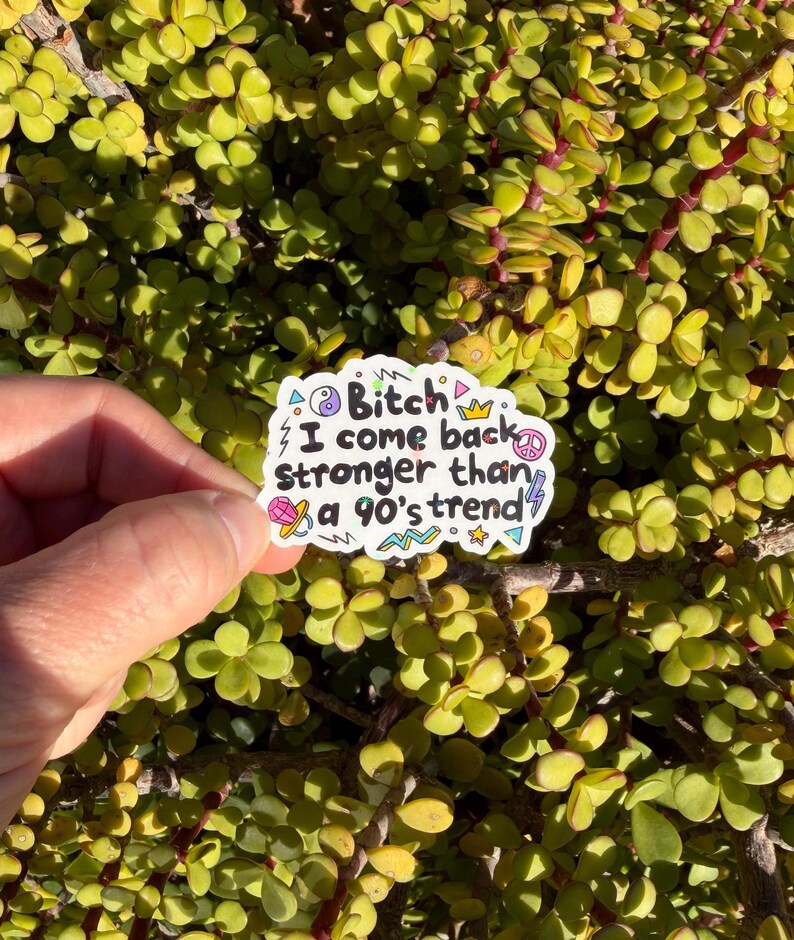 May include: A white die-cut sticker featuring the black text Bitch I come back stronger than a 90's trend surrounded by colorful illustrations of a yin-yang, crown, peace sign, lightning bolt, star, pacifier, and geometric zigzag shapes.