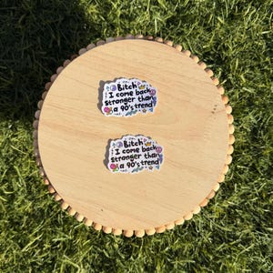 May include: Two white die-cut stickers featuring the black text "Bitch I come back stronger than a 90's trend" surrounded by colorful small graphic icons including a crown, lightning bolt, peace sign, and geometric shapes on a light wood surface.