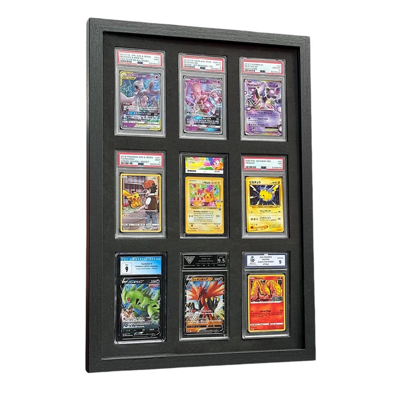Op de afbeelding: Een zwart omkaderde displaycase met negen beoordeelde Pok&eacute;mon-ruilkaarten. De kaarten bevatten verschillende personages en zijn ingekapseld in doorzichtige beschermhouders. Het frame is rechthoekig en heeft een donkere afwerking.
