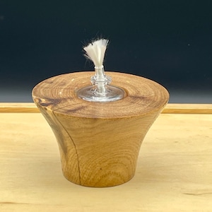 May include: A wooden oil lamp with a glass wick holder and a white wick. The lamp is sitting on a wooden surface.