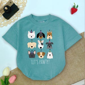 Pu&ograve; includere: Body da bambino turchese a maniche corte con un motivo di nove facce di cani dei cartoni animati con cappelli da festa. Il testo "LET'S PAWTY!" &egrave; stampato sotto. Il body &egrave; realizzato in materiale morbido.
