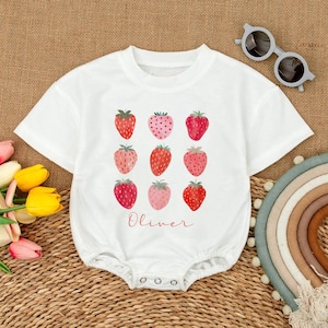 May include: White baby onesie with a red and pink strawberry pattern and the name "Oliver" printed on the front.