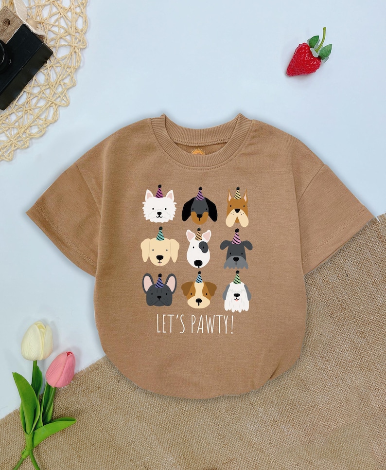 Pu&ograve; includere: Una maglietta a maniche corte color marrone chiaro con una grafica di nove facce di cani dei cartoni animati con cappelli da festa. Il testo "LET'S PAWTY!" &egrave; stampato sotto. La maglietta &egrave; in materiale morbido.
