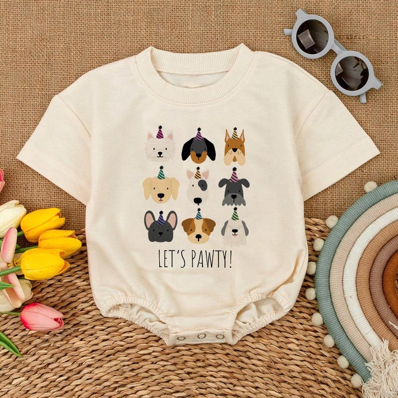 Pu&ograve; includere: Pagliaccetto per neonati color crema con girocollo e maniche corte. La parte anteriore presenta una grafica di vari volti di cani con cappelli da festa, con la scritta "LET'S PAWTY!" stampata sotto. Il pagliaccetto ha chiusure a scatto sul fondo.