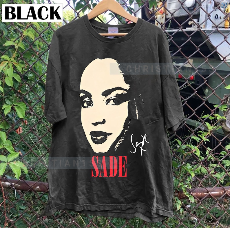 Może przedstawiać: Czarny T-shirt z czarno-białym obrazkiem Sade, piosenkarki, z jej podpisem pod obrazkiem. Tekst "SADE" jest czerwonymi literami pod podpisem.