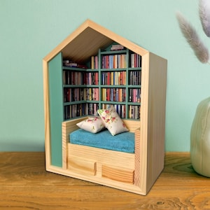 May include: A wooden bookshelf with a built-in couch and pillows. The bookshelf is filled with books and has a light green interior. The couch is covered in a blue fabric.