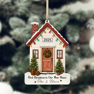 Pu&ograve; includere: Un ornamento natalizio a forma di casa con tetto rosso, camino in mattoni e luci a catena. L'ornamento presenta una porta rossa con una ghirlanda, due piccoli alberi di Natale e il testo "First Christmas in Our New Home - Peter & Maria" e l'anno 2025.
