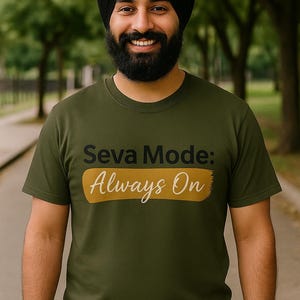 May include: Olive green t-shirt with the text "Seva Mode: Always On" in black and white. The text is above a gold horizontal brushstroke. The shirt is worn by a person with a black turban and beard.