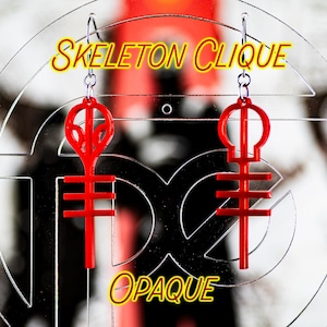 May include: Red opaque acrylic earrings with a skeleton clique symbol. The earrings are hanging from silver hooks.