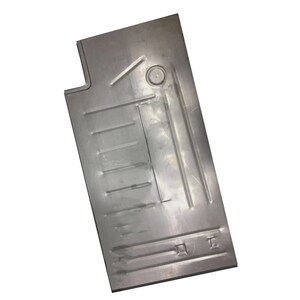 May include: A silver-colored metal panel with a rectangular shape and various stamped details. The panel has a circular indentation and several parallel lines, along with a small rectangular cutout and other geometric features.