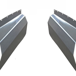 May include: Two silver-colored metal panels with a series of holes along the top edge. The panels have a geometric design with angled sides and a pointed bottom. The items are likely automotive parts.