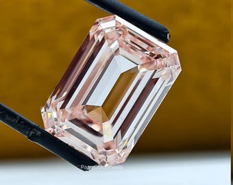 May include: A rectangular emerald-cut gemstone with a pale peach and light pink hue, featuring sharp facets that reflect light. The stone is held by black tweezers, and the text ParryGoldJewels is printed in small white letters at the base.