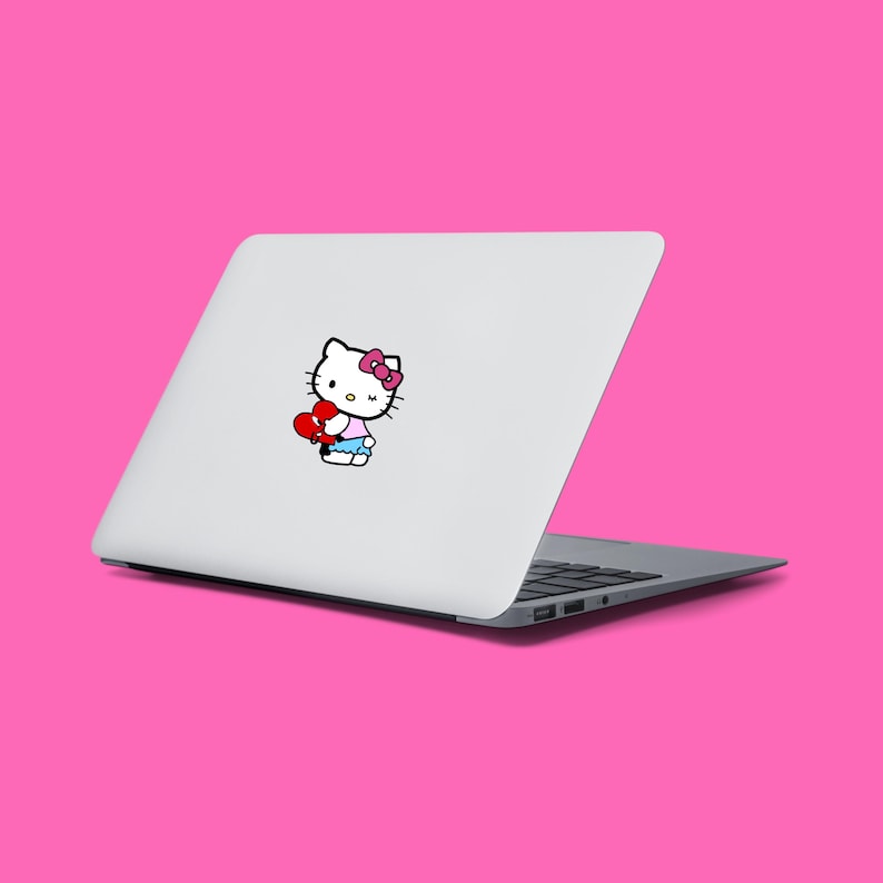 Puede incluir: Un port&aacute;til blanco con una pegatina de Hello Kitty en la tapa. La pegatina muestra a Hello Kitty sosteniendo un coraz&oacute;n rojo.