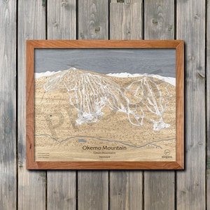 May include: A framed wooden map of Okemo Mountain in the Green Mountains of Vermont. The map shows the ski trails and lifts. The text "Okemo Mountain", "Green Mountains", and "Vermont" is printed below the map. The text "slopes." is printed in the lower right corner.