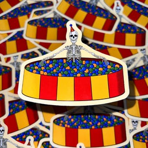 May include: A skeleton wearing a party hat is sitting in a yellow, red, and white striped ball pit filled with blue, green, and yellow balls. The ball pit is on a white background.