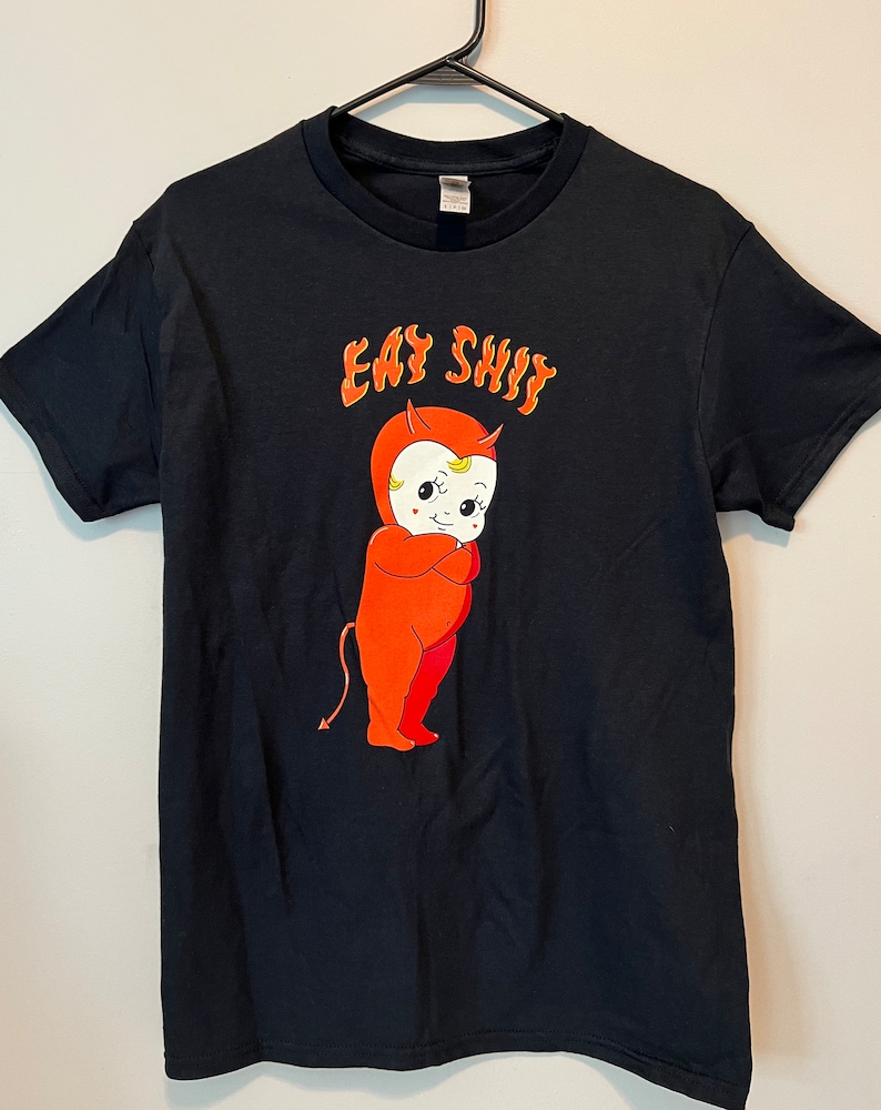 以下が含まれることがあります： オレンジ色の炎の中に「Easy Shit」という文字と、赤い悪魔の赤ちゃんが描かれた黒いTシャツです。