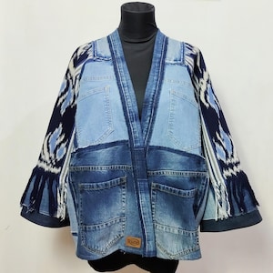 Könnte beinhalten: Eine Patchwork-Jeansjacke mit einzigartigem Design. Die Jacke hat verschiedene Blautöne, Taschen und einen Fransenbesatz an den Ärmeln. Die Ärmel haben einen gemusterten Stoff mit blauen und weißen Akzenten. Auf der Jacke befindet sich das Wort "Ruzo" auf einem kleinen Aufnäher.