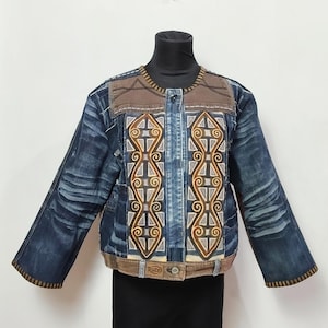 May include: A denim jacket featuring dark blue distressed sleeves and a central panel with brown and grey geometric patterns. The garment includes brown fabric accents at the shoulders and hem, a single button closure, and a small Ruze brand label.