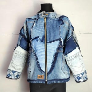 Può includere: Giacca in denim patchwork in varie tonalità di blu. La giacca presenta un collo alto, una cerniera dorata e un mix di pezzi di denim cuciti insieme. Le maniche hanno polsini decorativi con un motivo floreale. Una piccola etichetta marrone recita "Ruze".