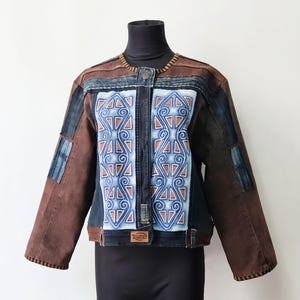 Könnte beinhalten: Eine braune und dunkelblaue Jeansjacke mit einem Mittelteil, das ein hellblaues und weißes geometrisches Spiralmuster aufweist. Die Jacke hat einen Rundhalsausschnitt, lange Ärmel mit dunkelblauen Einsätzen und ein braunes Etikett mit Ruze.