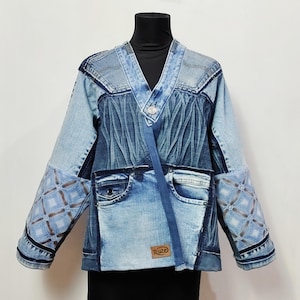 Pode incluir: Casaco de ganga patchwork com decote em V. O casaco apresenta vários tons de ganga azul, costuras decorativas e patches estampados nas mangas. Uma pequena etiqueta com a palavra "Ruze" é visível.