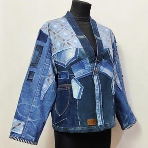 Puede incluir: Chaqueta vaquera patchwork en varios tonos de azul. La chaqueta presenta un diseño único con patrones geométricos y múltiples parches de mezclilla. Tiene cierre de botón y un pequeño bolsillo. La chaqueta se exhibe en un maniquí negro.