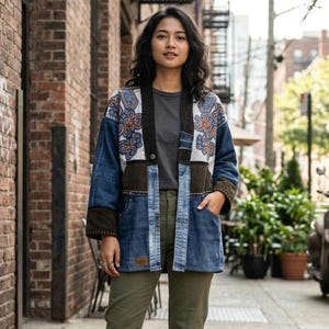 May include: A patchwork jacket constructed from blue denim and brown fabric panels. The garment features a white upper section with intricate blue and orange embroidery, a single button closure, two front pockets, and a small rectangular brown brand patch.