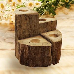 Puede incluir: Un portavelas rústico de madera con cuatro aberturas circulares para velas. El soporte está hecho de secciones de un tronco de árbol, con un acabado natural y texturizado. El diseño es escalonado, creando una pieza decorativa única.