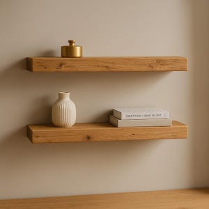 Puede incluir: Dos estantes flotantes de madera con objetos. El estante superior tiene un pequeño recipiente dorado. El estante inferior tiene un jarrón blanco y dos libros. Los libros tienen el texto "EVERYTHING I WANT TO EAT".
