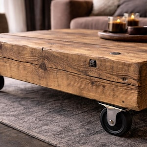 Könnte beinhalten: Ein rustikaler, rechteckiger Couchtisch aus Altholz. Der Tisch hat eine natürliche Holzmaserung und ist auf vier schwarzen Rollen montiert. Der Tisch hat eine warme braune Farbe und befindet sich in einem Wohnzimmer.