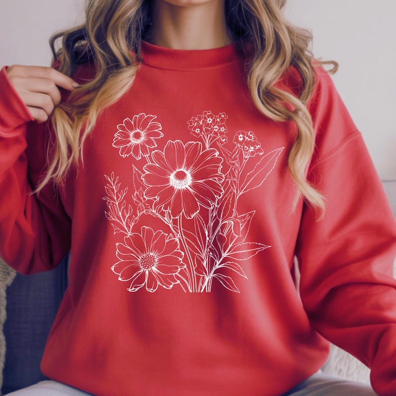 May include: A red sweatshirt featuring a white floral design. The graphic includes detailed outlines of daisies and other flowers. The sweatshirt has a crew neck and long sleeves, perfect for casual wear.