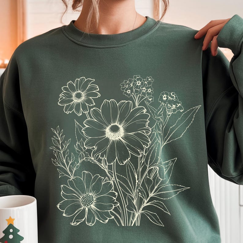 May include: Dark green sweatshirt featuring a white floral design. The graphic includes detailed outlines of daisies and other flowers with leaves. The crew neck sweatshirt is a solid color and has a relaxed fit.