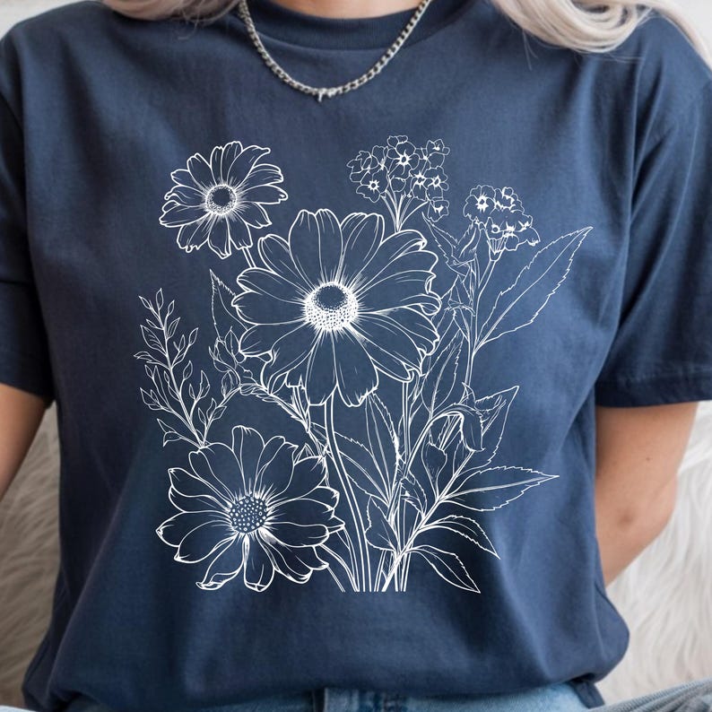 May include: Navy blue t-shirt featuring a white floral line art design. The design includes detailed outlines of daisies, other flowers, and leaves. The shirt is a comfortable, casual style.