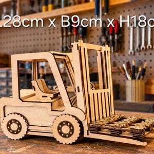 May include: A light-colored wooden model of a forklift featuring a seat, a mast, and a small pallet on the forks. The text L28cm x B9cm x H18cm is visible above the model, indicating its dimensions in centimeters.