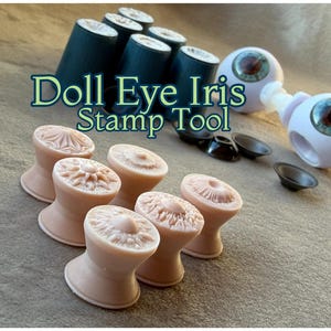 以下が含まれることがあります： 画像には、人形の目の虹彩スタンプツールと人形の目が表示されています。ツールは、さまざまな花柄と幾何学模様のライトブラウンです。人形の目は、青と茶色の虹彩を持つ白です。「Doll Eye Iris Stamp Tool」というテキストが画像に表示されています。
