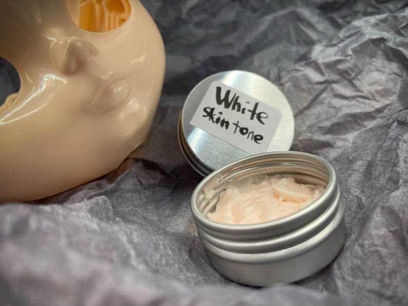 May include: A small, silver tin with a white label that reads "White Skin Tone". The tin is open and contains a pink, creamy substance.