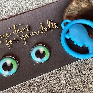 May include: Two blue and green glass eyes with black pupils and a blue plastic silhouette of a person's head in a circle.