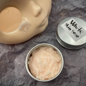 May include: A small silver container with a white label that says "White skin tone" and a pink cream inside.
