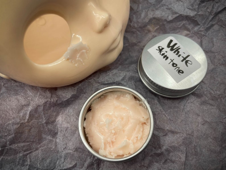 May include: A small silver container with a white label that says "White skin tone" and a pink cream inside.