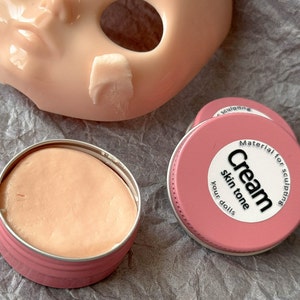 May include: Two pink containers of sculpting cream for dolls. One container is open and shows the pink cream inside. The other container has a white label that reads "Material for sculpting Cream skin tone your dolls".
