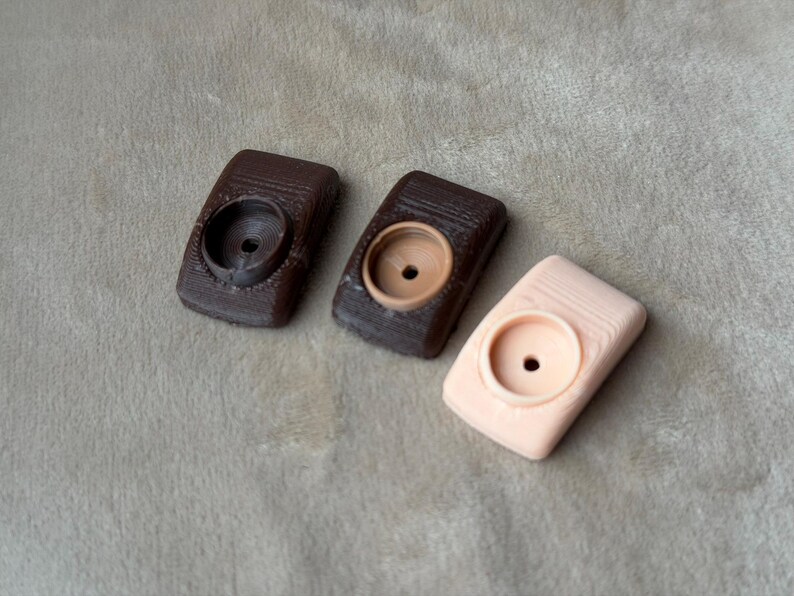 Może przedstawiać: Trzy małe, prostokątne, dekoracyjne przedmioty z okrągłym wgłębieniem. Dwa są ciemnobrązowe, a jeden jasnor&oacute;żowy. Przedmioty ułożone są na jasnoszarej, teksturowanej powierzchni.