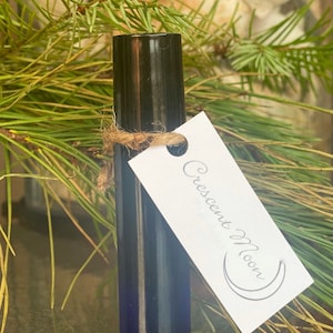 May include: A small, dark blue glass roller bottle with a black cap and a white label that says "Crescent Moon" with a crescent moon symbol.