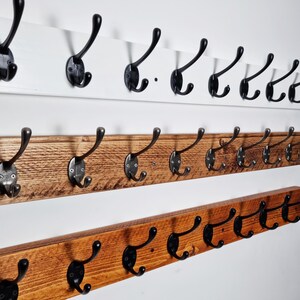 May include: Three wooden coat racks with black metal hooks. The top rack is white, the middle rack is brown, and the bottom rack is a darker brown.