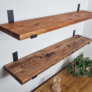May include: Two wooden shelves with black metal brackets mounted on a white wall. The shelves are made of reclaimed wood and have a rustic finish.