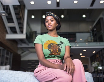 Puede incluir: Una mujer con una camiseta verde con un gráfico de una mujer negra con una puesta de sol y palmeras de fondo. El texto de la camiseta dice "I'm a Queen, Better Not Forget It".