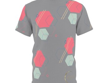Puede incluir: Una camiseta gris con un patrón geométrico que presenta hexágonos rosas y azules y líneas. La camiseta tiene un pequeño logotipo circular dorado con el texto "Golden Girl" en una fuente cursiva.