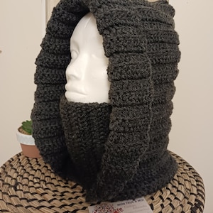 Könnte beinhalten: Ein dunkelgrauer, gehäkelter Kapuzen-Schal mit einem dicken, strukturierten Design. Der Schal ist umgeklappt und über einen Mannequin-Kopf gelegt.