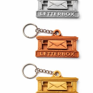 Può includere: Tre portachiavi in metallo a forma di cassetta delle lettere in argento, bronzo e oro. Ogni portachiavi presenta un design di cassetta delle lettere in miniatura con una busta e la scritta "LETTERBOX" in basso. I portachiavi hanno un anello e una catena.