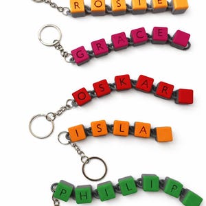 May include: Keychains with names spelled out in colorful letter blocks. The names include "Rosie", "Grace", "Oskar", "Isla", and "Philip". Each keychain has a silver ring and chain.