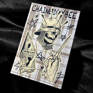 May include: A rectangular sticker with a tattoo-style design. The design features a skull wearing a helmet, a hand holding a dagger, and a tower. The text "CHAINED BEE" is at the top. The background has a grid pattern with star shapes.